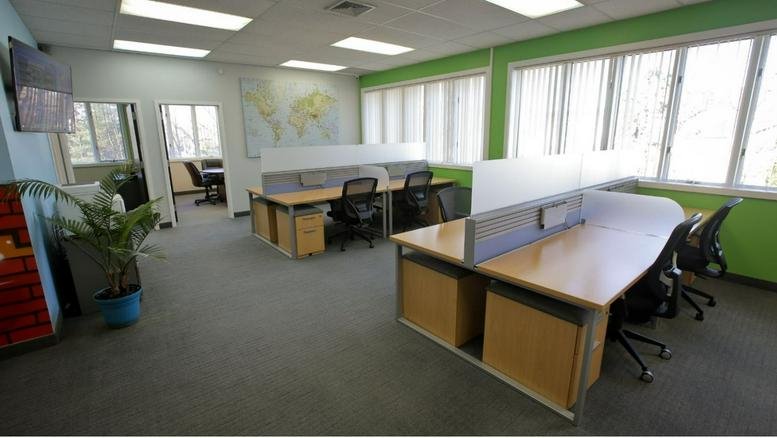 Open-plan office space with multiple desk clusters, world map wall art, and green accent walls.
