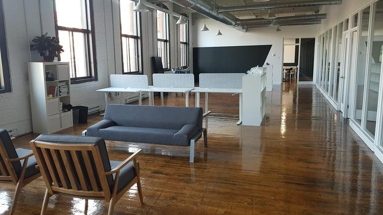Spacious open-plan workspace at 4020 Rue Saint-Ambroise No. 495 with polished wood floors and a grey lounge sofa.