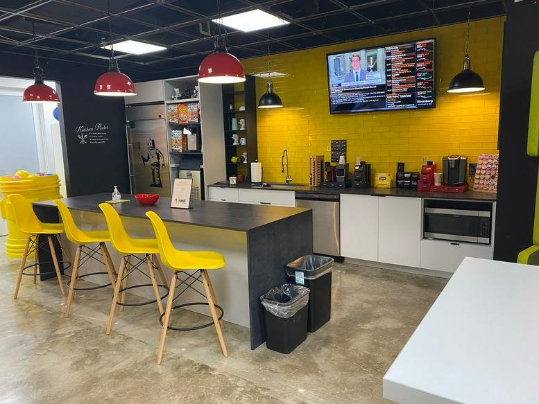 Modern communal kitchen with yellow stools, red pendant lights, and a wall-mounted TV.