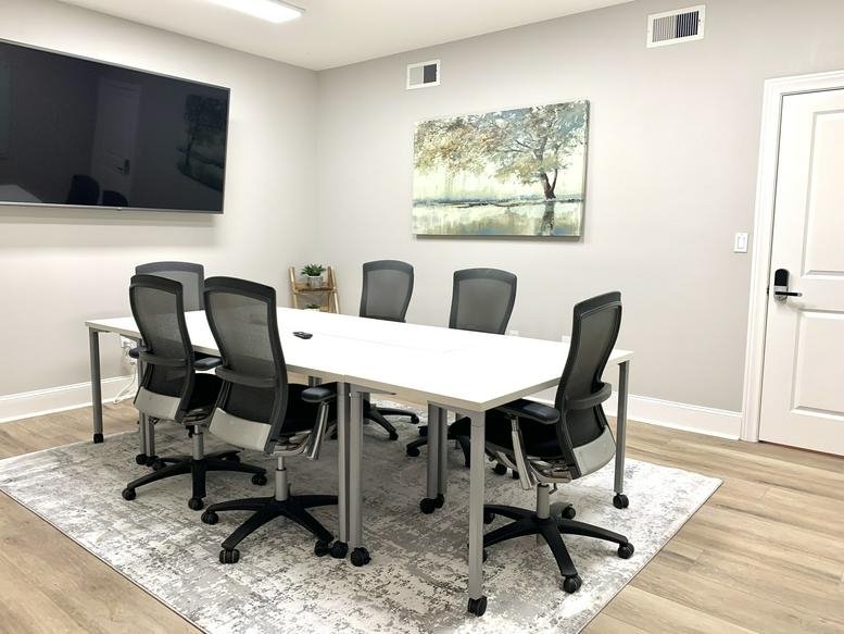 Bright conference room with a long white table, black chairs, and landscape wall art.