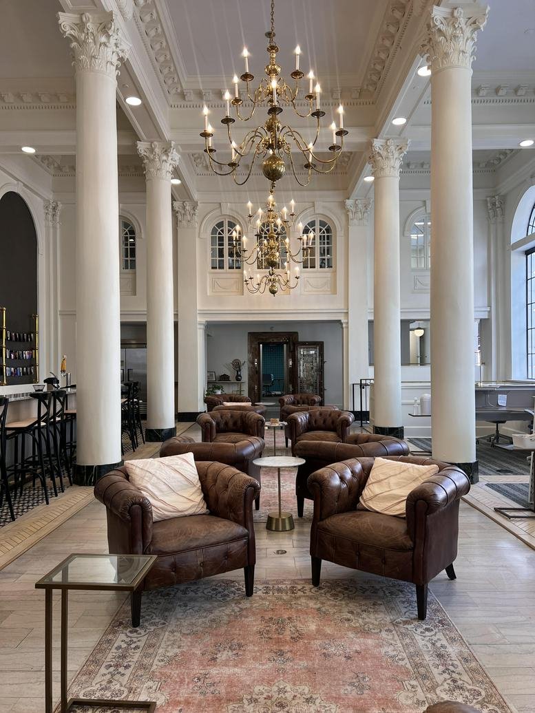 Grand lobby lounge with tall columns, ornate chandeliers, and leather Chesterfield armchairs.