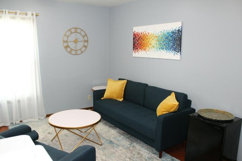 Spacious seating area at 5842 Main Street, Suite 2B with a blue sofa, yellow pillows, and colorful wall art.