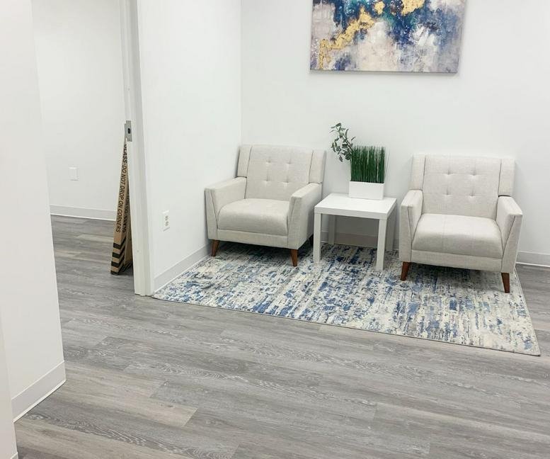 Bright reception waiting area at 7004 Security Boulevard, Suite 300 with white armchairs and abstract art.