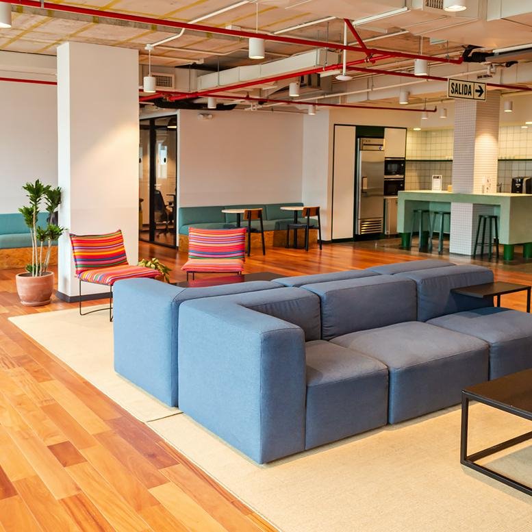 Spacious communal lounge at 755, Juan De Arona featuring a blue modular sofa, striped chairs, and wooden floors.