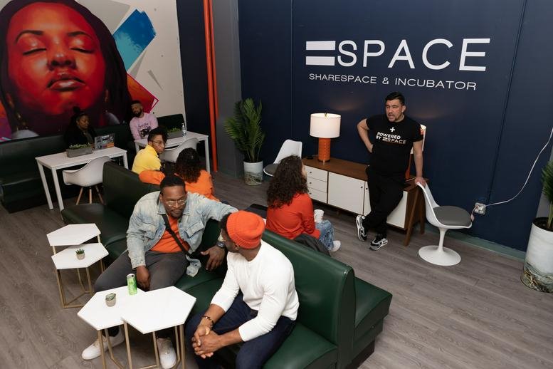 Communal lounge with a colorful mural, green leather seating, and people socializing.