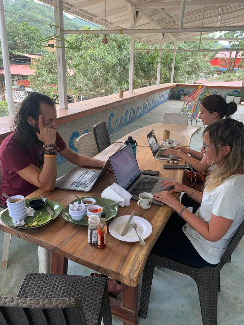 Outdoor workspace with professionals using laptops on a long wooden table with mountain views.