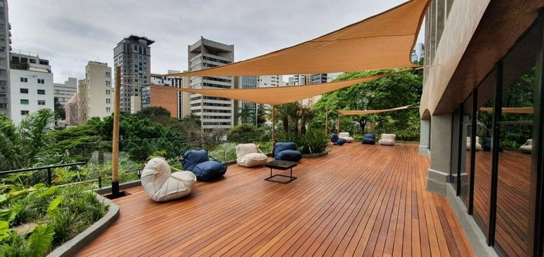 Outdoor wooden deck lounge with comfortable beanbags and large sun sails overlooking city greenery.