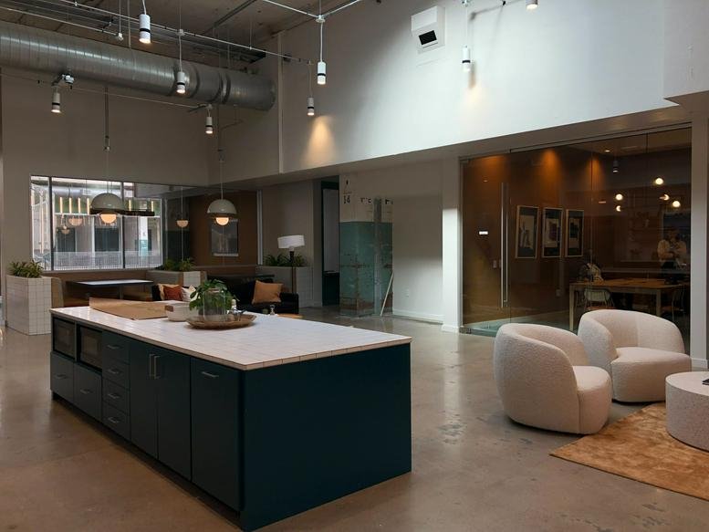 Spacious communal lounge at POST Houston with a kitchen island, modern white armchairs, and high ceilings.