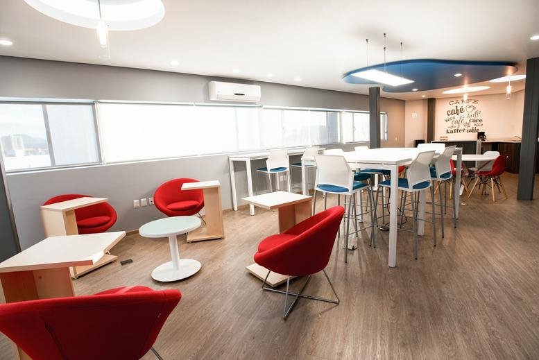 Spacious communal lounge featuring red modern chairs and a large white high-top table.