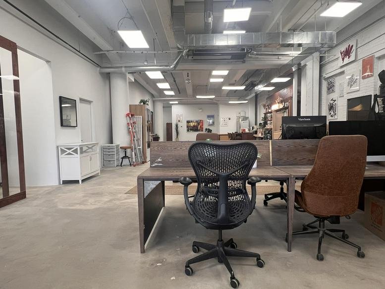 Modern open-plan office area with rows of desks, ergonomic chairs, and industrial ceiling details.
