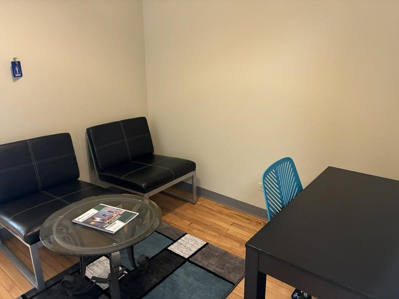 Waiting area at 111 North Wabash Avenue with black leather seating, a glass coffee table, and a colorful rug.