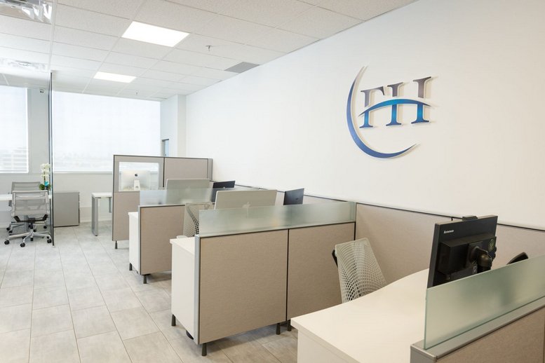 Open-plan office space with neutral-toned cubicles and a branded wall logo.