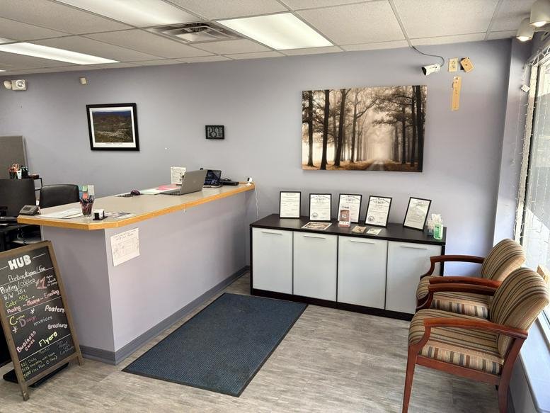 Reception area with a grey front desk, waiting chairs, and wall art of a misty forest.