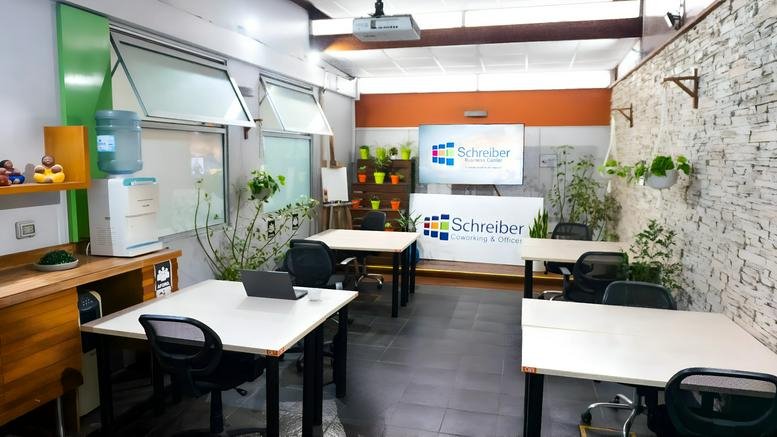 Bright coworking space featuring white desks, green feature walls, and indoor plants.