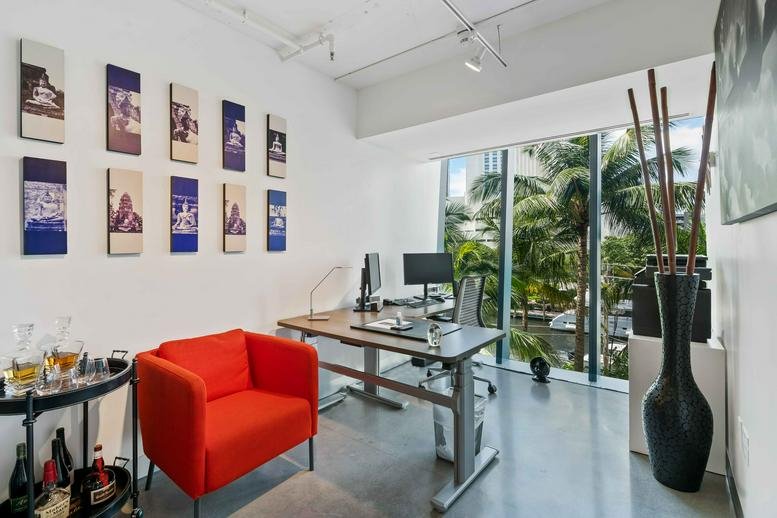 Modern workspace featuring an orange armchair and large windows with palm tree views.