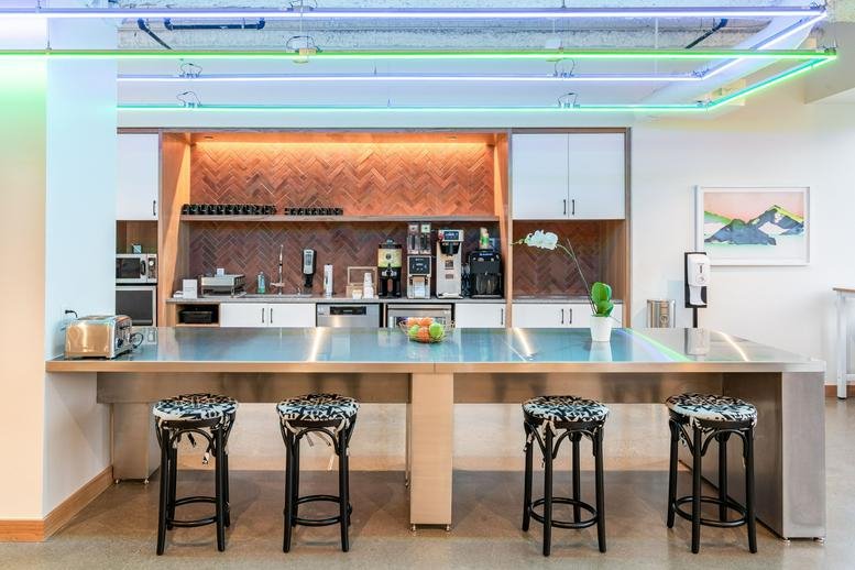 Modern communal kitchen area at 400 Capitol Mall with a long stainless steel island and bar stools.