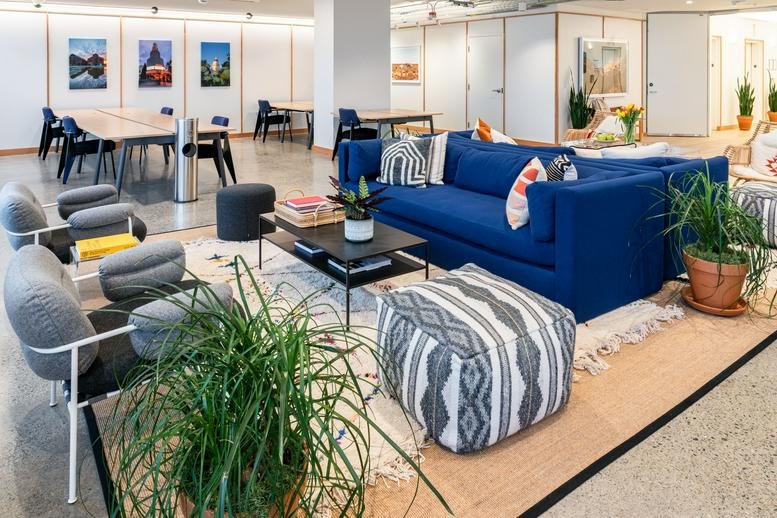 Bright coworking lounge at 400 Capitol Mall featuring a blue velvet sofa and patterned ottomans.