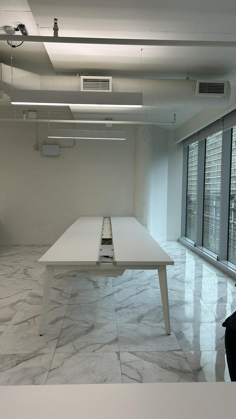 Bright open-plan workspace at Saint Thomas Street, Yorkville, Toronto with a long white desk and marble-patterned floors.