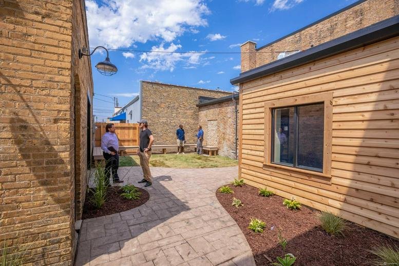 Outdoor patio space with brick and wood siding, featuring seating and greenery.