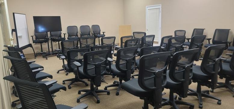 Classroom-style training room at 2311 North Tracy Boulevard Suite A with rows of black mesh chairs and a large screen.