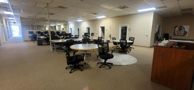 Wide view of a brightly lit open-plan coworking area with round tables and various workstations.