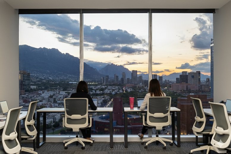 Professional desks facing a large window with a panoramic mountain and city sunset view.