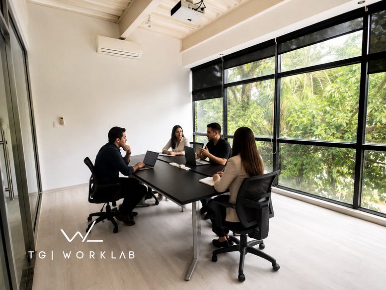 Meeting room with four people collaborating at a black table overlooking lush green trees at Plaza Altum Center.