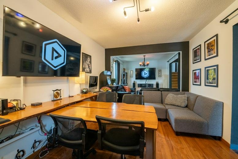 Communal break area with a large wooden table, corner sofa, and wall-mounted TV.