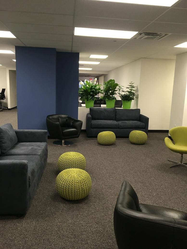 Modern lounge area featuring blue sofas, a black armchair, and lime green knitted ottomans.