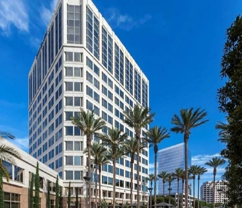 Exterior view of the white high-rise facade of 100 Spectrum Center Drive under a bright blue sky.