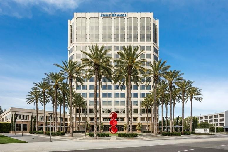 Symmetrical exterior view of a white office building framed by rows of tall palm trees.