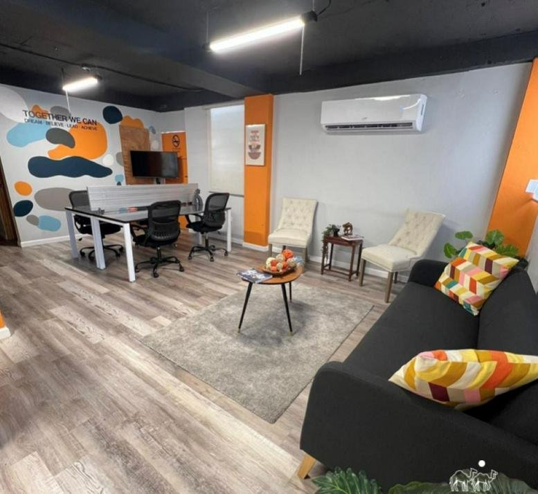 Vibrant communal lounge area with a dark sofa, colourful accent pillows, and an abstract mural.