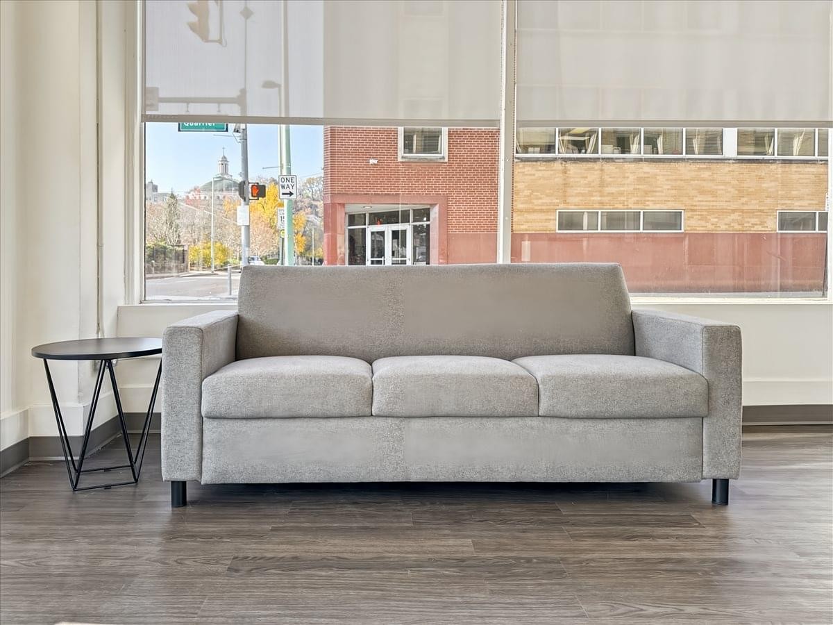 Lounge area at 1030 Quarrier Street, Suite 100 featuring a grey sofa, side table, and large windows with street views.