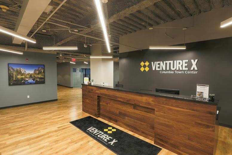 Modern reception area with a dark wood desk and Venture X branding.