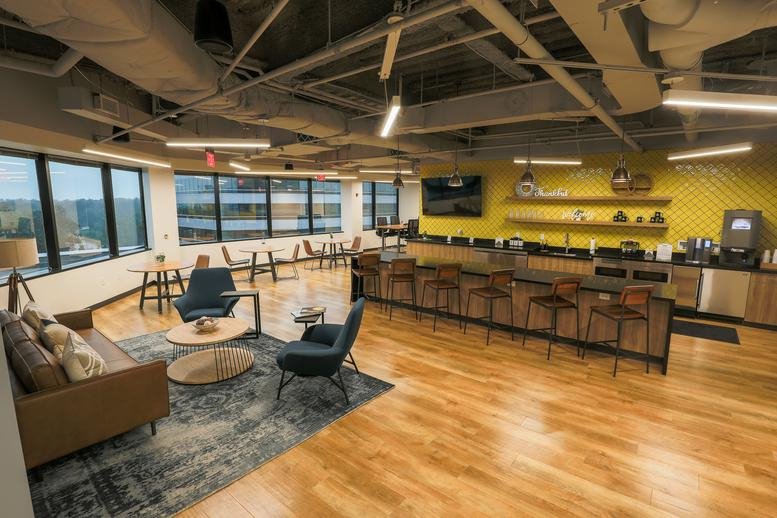 Spacious breakout area featuring a yellow tiled wall, cafe seating, and a kitchenette.