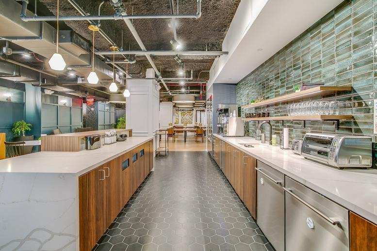 Spacious communal kitchen area at 11 West 42nd Street with wood cabinets and a long marble island.