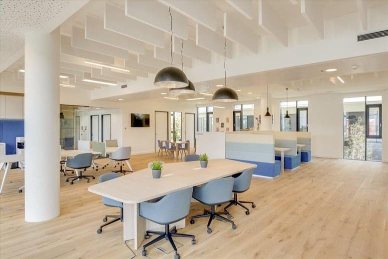 Open-plan coworking space with high ceilings, pendant lighting, and various seating zones.