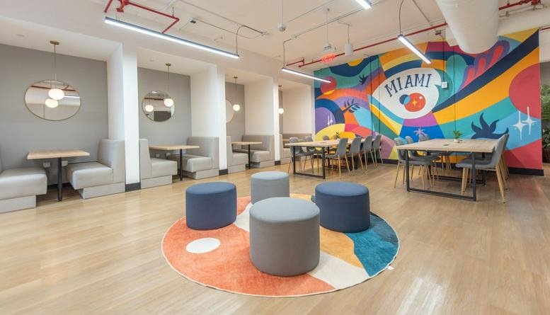Vibrant coworking zone with colorful floor rugs, blue stools, and a graphic wall mural.