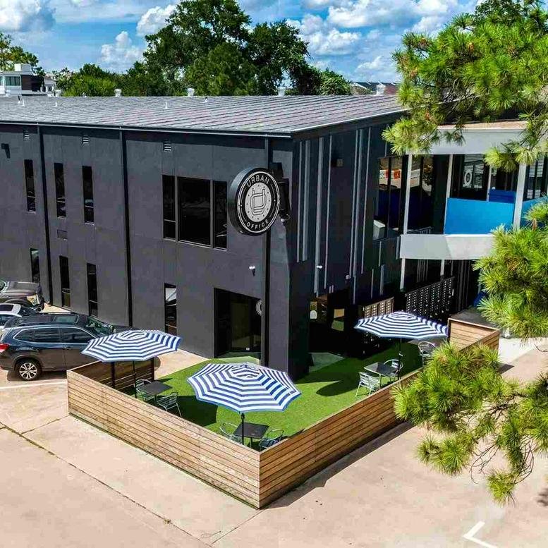 Exterior view of the dark-facade building at 1100 West 23rd Street featuring a patio with striped umbrellas.