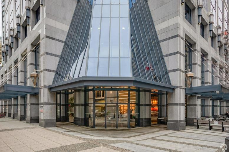 Building entrance with a modern glass-peaked canopy and stone pillars.