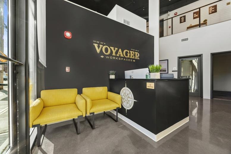 Modern reception desk with a compass logo and yellow lounge chairs.