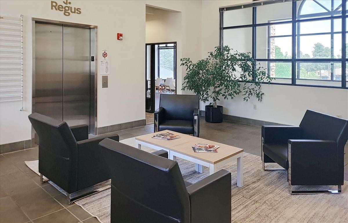 Lobby at 1120 West University Avenue featuring a modern elevator, black leather armchairs, and a large plant.