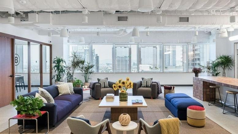 Spacious communal lounge at 1150 South Olive Street with blue sofas, potted plants, and city skyline views.