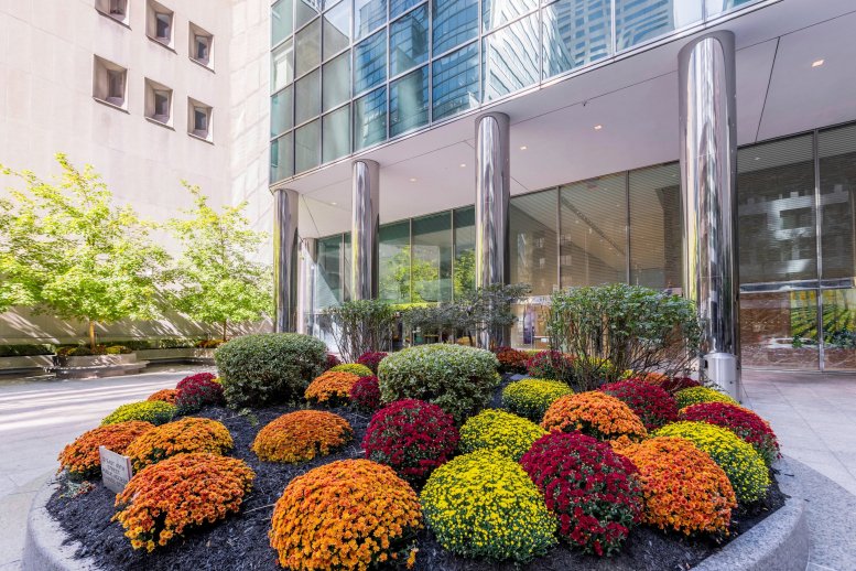 Exterior entrance of Tower 49 at 12 E 49th St featuring polished columns and vibrant flower beds.