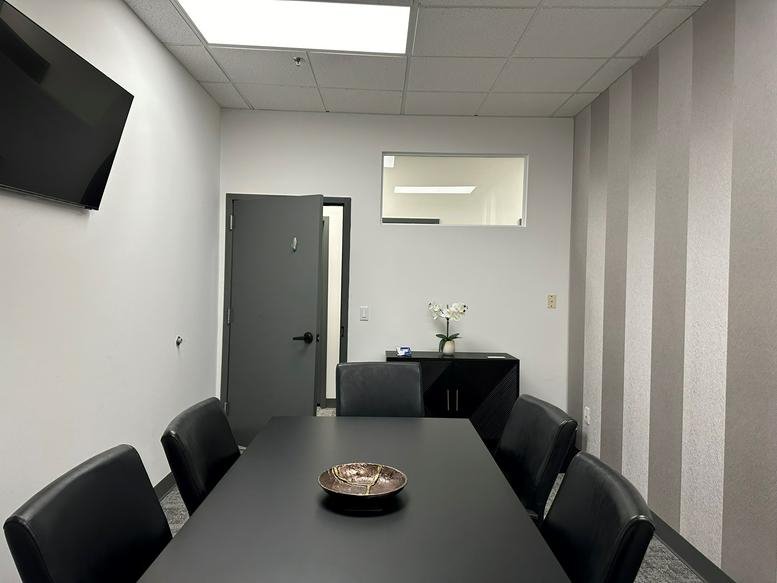 Meeting room with a long black table, leather chairs, and a grey striped feature wall.