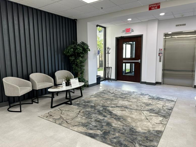 Spacious lobby at 12 Penns Trail with grey armchairs, a patterned rug, and a modern accent wall.