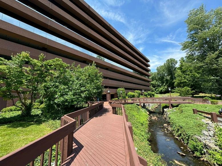 Exterior of the terraced brown building at 120 White Plains Road featuring a wooden walkway over a stream.