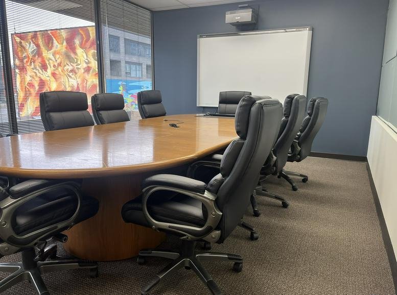 Spacious boardroom with a large wood table and black leather chairs.