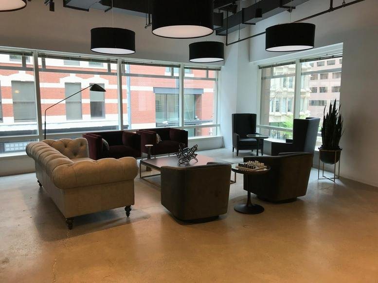 Wide-angle common area at 125 High Street, 2nd Floor, with tufted sofas and large windows showing city views.