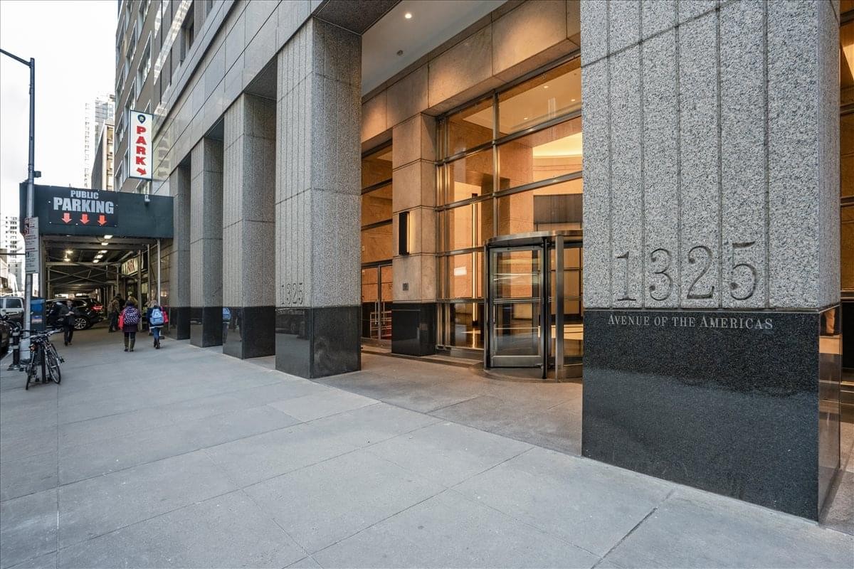 Exterior entrance of 1325 Avenue of the Americas featuring a stone facade and glass doors.